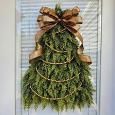 a christmas tree made out of evergreen branches with brown bows and pearls hanging on the front door