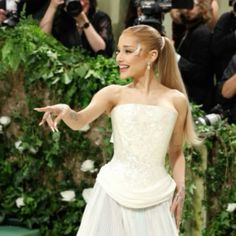 a woman in a white dress pointing at something on the ground with cameras around her