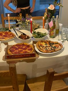 a woman standing in front of a table filled with pizzas and other food items