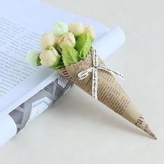 a paper cone with flowers tied to it sitting next to an open book