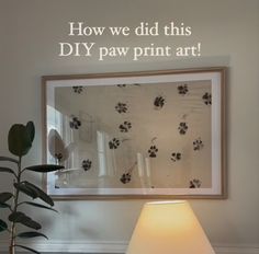 a lamp sitting on top of a table in front of a framed picture with paw prints