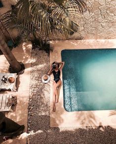 a woman in a bathing suit sitting on the edge of a pool next to a palm tree