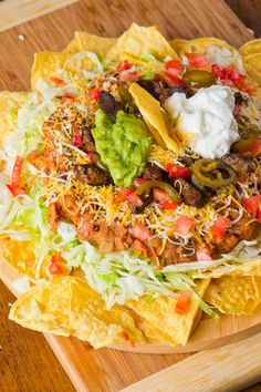 nachos with cheese, lettuce and tomatoes on a wooden platter