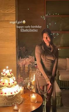 a woman standing in front of a birthday cake with candles on the table next to it