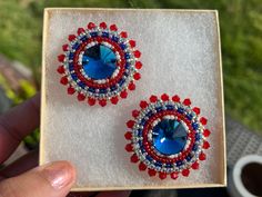 two red, white and blue beaded earrings in a box with grass behind it