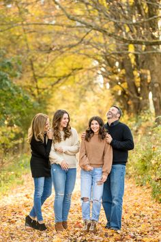 three adults and one child standing in the leaves with their arms around each other smiling