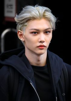 a young man with blonde hair wearing a black hoodie and looking at the camera