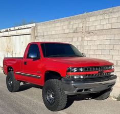 a red pickup truck parked in front of a brick wall on the side of a road