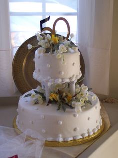 a three tiered cake with white flowers on the top and gold trimmings