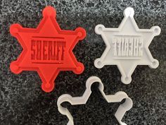 three cookie cutters shaped like police badges on a counter top with the word sheriff written in red and white