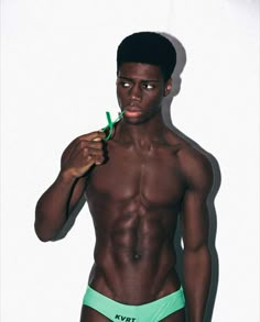 a shirtless man is brushing his teeth with a green toothbrush while standing in front of a white wall