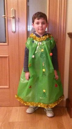 a young boy wearing a green dress standing in front of a door with a christmas tree on it