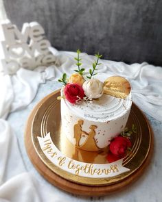 a white and gold wedding cake with red roses on top, sitting on a plate