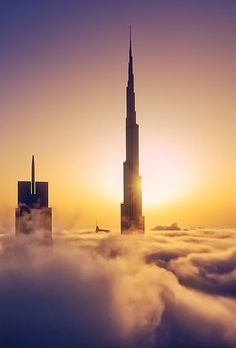 the burj building is surrounded by clouds in the sun setting over the city