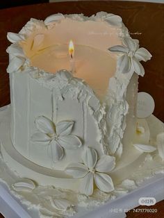 a white cake sitting on top of a table with a lit candle in the middle