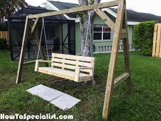 a wooden swing set in front of a house with a tree and grass area next to it