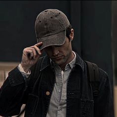 a man wearing a hat while talking on a cell phone in the street with his hand to his ear