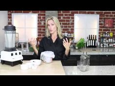 a woman standing in front of a blender on top of a counter next to cups