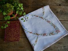 a table with a book and a plant on it next to a white cloth that has been embroidered onto