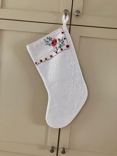 a white christmas stocking hanging from the side of a kitchen cabinet with red flowers on it