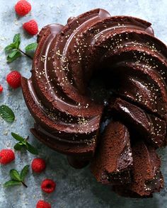 a chocolate bundt cake with raspberries around it on a blue table top