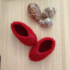 two crocheted red slippers sitting on top of a bamboo mat next to sea shells