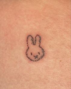 a small rabbit tattoo on the back of a woman's shoulder, with black ink