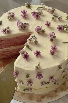 a cake with white frosting and pink flowers on it is being cut by a knife