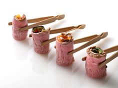 five sushi rolls with chopsticks sticking out of them on a white surface