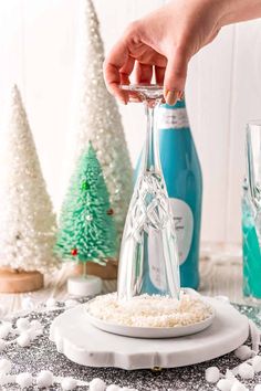 someone is pouring wine into a bottle with snow on the ground next to christmas trees