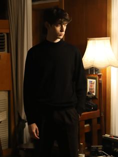 a young man standing in a living room next to a lamp