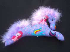 a stuffed toy horse laying on top of a black surface with pink and blue feathers