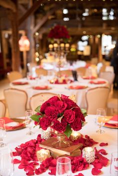 the centerpieces on this table are red roses and candles, with gold accents