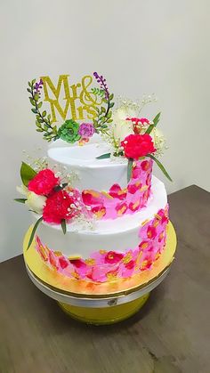 a three tiered cake with flowers on the top and mr and mrs written in gold