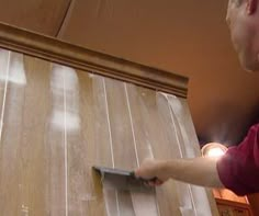 a man is using a paint roller to paint the wood paneling on a wall