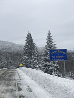 a blue sign sitting on the side of a road next to snow covered evergreen trees