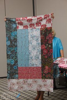 a woman holding up a large quilt in an office