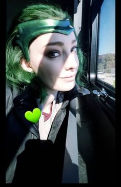 a woman with green hair and black jacket looking out the window on a train or bus