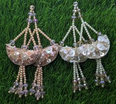 two brooches are laying on the grass with pearls and beads hanging from them