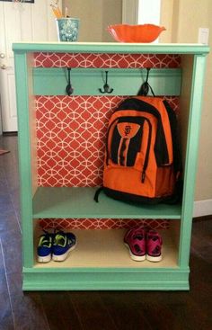 an orange backpack is hanging on a green shelf next to some shoes and a bowl