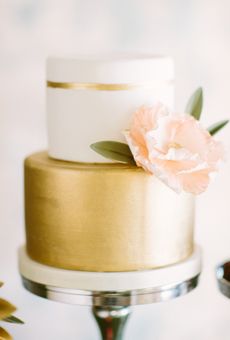 a white and gold wedding cake with a flower on top is sitting on a table