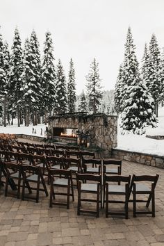 rows of wooden chairs sitting in front of a stone fireplace surrounded by snow covered trees