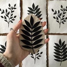 a hand holding a piece of paper with black leaves on it in front of four white tiles