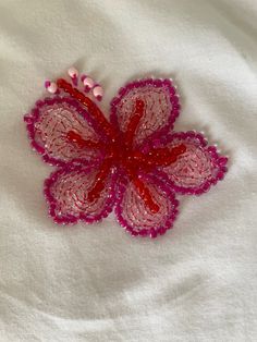 a close up of a pink flower on a white cloth with bead work in the middle