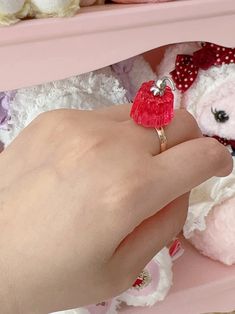 a person's hand holding a ring with a heart on it in front of stuffed animals