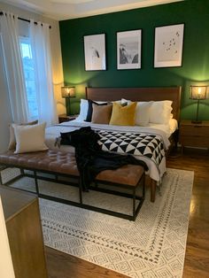 a bedroom with green walls, white and black bedding, brown foot stools, and pictures on the wall