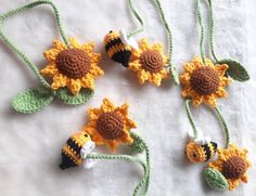 four crocheted sunflowers and two bees on a white sheet with green leaves