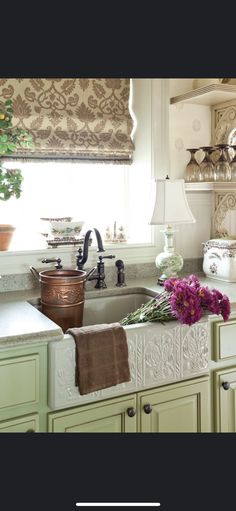 a kitchen with green cabinets and pink flowers on the window sill in front of the sink