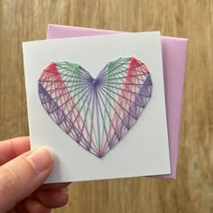 a hand holding up a card with a heart shaped string art design on the front