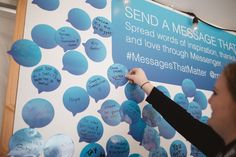 a woman writes messages on a sign in front of a wall with blue speech bubbles